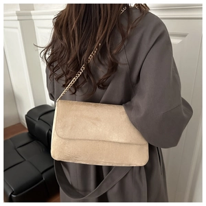 Detail of apricot suede crossbody bag featuring gold chain strap on model's shoulder