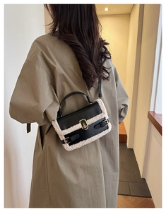 Detail of crossbody bag with black faux leather and cream shearling trim on camel coat