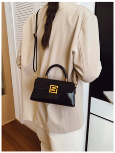 Detail of black leather handbag featuring a golden square buckle and adjustable strap