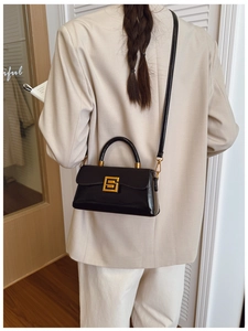 Detailed view of black patent leather crossbody bag with a distinctive golden S-buckle