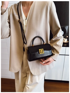 Detail of a black leather rectangular handbag with a gold buckle worn with a beige suit