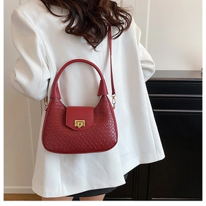 Detail of burgundy woven leather half-moon bag with gold twist lock on white blazer