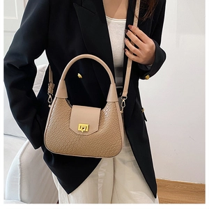 Close-up of beige crocodile pattern handbag with gold clasp on black suit background
