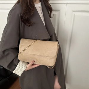 Minimalist beige suede crossbody bag with gold chain strap worn with a grey trench coat