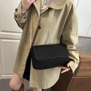 Suede crossbody bag in black with gold chain strap worn over a khaki trench coat