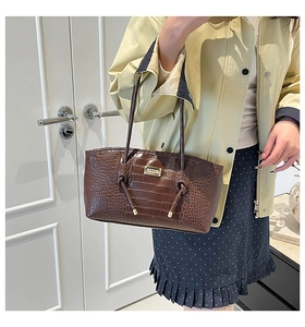 Detail of dark brown croc-effect shoulder bag with gold logo and knotted strap details