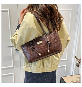 Detail of dark brown croc-textured tote bag with knotted shoulder strap and metal plate