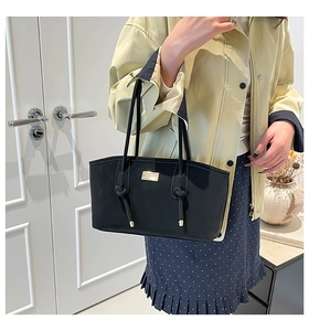 Detail of minimalist black tote bag with gold metal plate and knotted tassel decoration