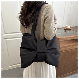 Model wearing a black nylon shoulder bag featuring a large decorative bow design