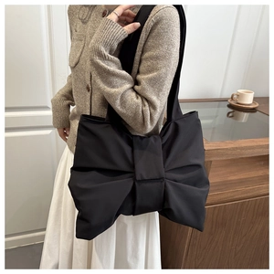 Modern black nylon tote bag featuring a large decorative bow design worn by a model