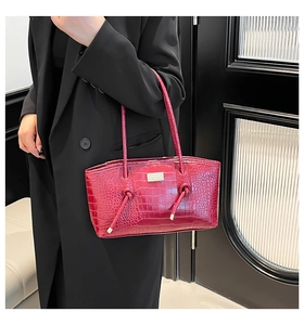 Detail of burgundy crocodile pattern tote bag with knotted shoulder strap and metal logo