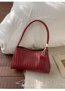 Gros plan détaillé du sac bandoulière en cuir tressé rouge foncé sur fond épuré