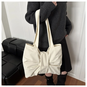 Detail of a large bow-knot design on a cream nylon shoulder bag shown on a model