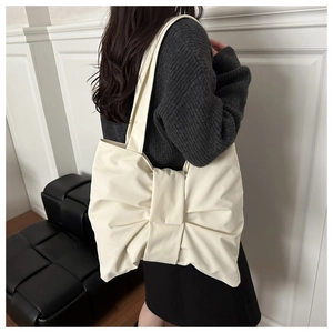 Detail of an off-white tote bag featuring a large decorative bow and soft faux leather texture