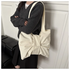 Detail of a creamy white leather shoulder bag featuring a large decorative bow design