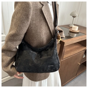 Sac à bandoulière demi-lune noir porté avec un blazer marron et une robe blanche