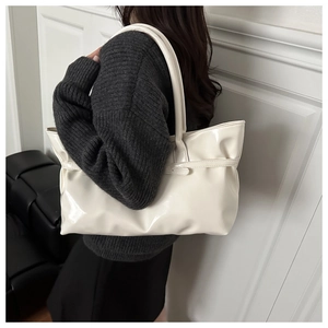 Gros plan d'un sac cabas en cuir verni blanc crème porté à l'épaule par un mannequin élégant