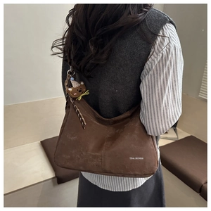 Close-up of brown suede hobo bag with teddy bear charm and logo text detail