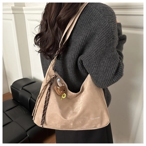 Detail of beige suede tote bag featuring a cute teddy bear charm and woven tassel detail