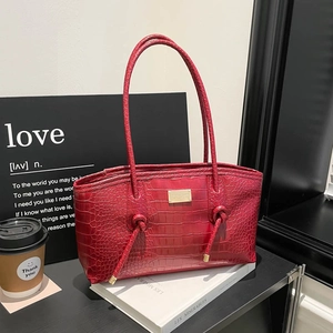Red crocodile pattern tote bag with gold logo and knotted handles on white books
