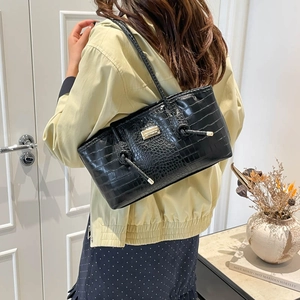 Classic black crocodile pattern tote bag with gold hardware worn by a model in a room