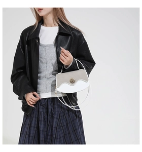 Detail of a wave-patterned shoulder bag with gold twist lock worn by a model