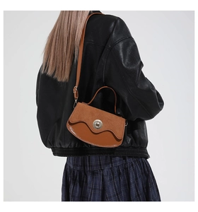 Brown leather crossbody bag with metal twist lock shown on model wearing black leather jacket