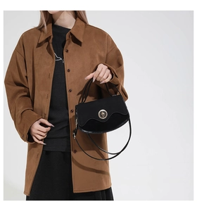Detail of black crossbody bag with wavy flap design and circular gold metal clasp