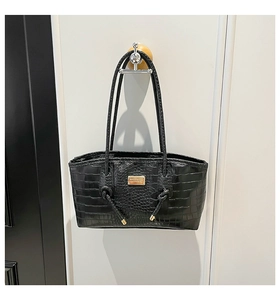 Detail of black crocodile texture leather tote bag with rectangular gold metal logo plaque