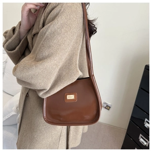 Detailed view of dark brown faux leather shoulder bag with gold logo plaque