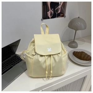 Detail eines cremefarbenen Mini-Rucksacks mit Kordelzug und Logo in gemütlichem Ambiente