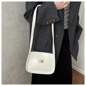 Detail of a creamy white glossy patent leather shoulder bag with a metal logo plate