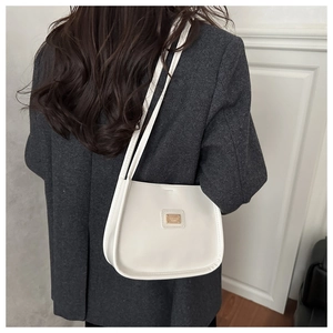 Detail view of a creamy white leather shoulder bag with gold metal plaque on a grey blazer