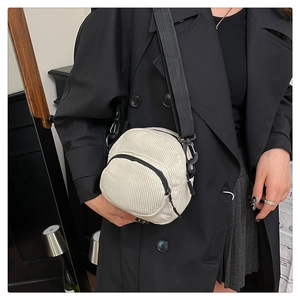 Detail of a beige corduroy crossbody shell bag worn over a black winter coat