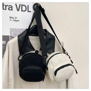 Detail of corduroy crossbody bags in black and off-white on a beige trench coat
