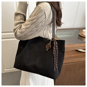 Detail of black suede tote bag featuring leather strap and woven tassel pendant