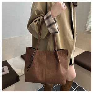 Close-up of caramel suede tote bag featuring a decorative woven pendant and stitched seam