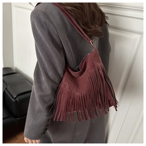 Détail du sac cabas en daim bordeaux avec franges porté à l'épaule dans un intérieur