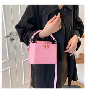 Sac seau rose à texture litchi et logo doré porté sur un long manteau noir