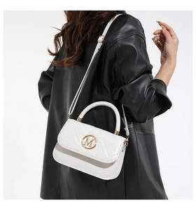 Detail view of white quilted crossbody bag featuring a golden M logo and metal hardware