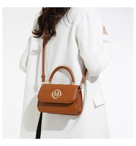 Détail d'un sac bandoulière matelassé caramel avec logo M doré sur veste blanche