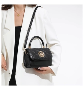 Detail of black quilted leather crossbody bag with gold M logo on white blazer model
