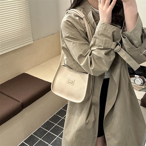 Elegant beige faux leather baguette shoulder bag with gold logo on stylish model