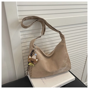 Close-up of khaki suede shoulder bag with a cute bear charm on a white book