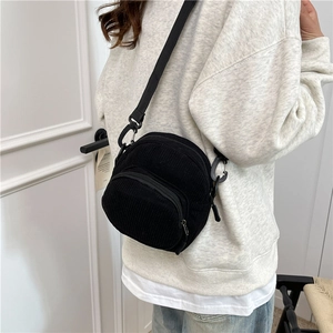 Minimalist black corduroy shell-shaped crossbody bag with adjustable strap and front pocket