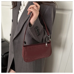 Détail d'un sac baguette en daim bordeaux avec fermeture éclair porté sur un blazer