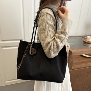 Large black suede bucket bag with brown straps and fringe detail shown on a model