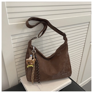 Detailed close-up of brown suede crossbody bag with bear pendant on white book