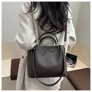 Dettaglio di borsa tote in pelle martellata marrone scuro indossata su un cappotto