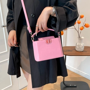 Sac bandoulière rose structuré en cuir avec logo doré porté par un mannequin